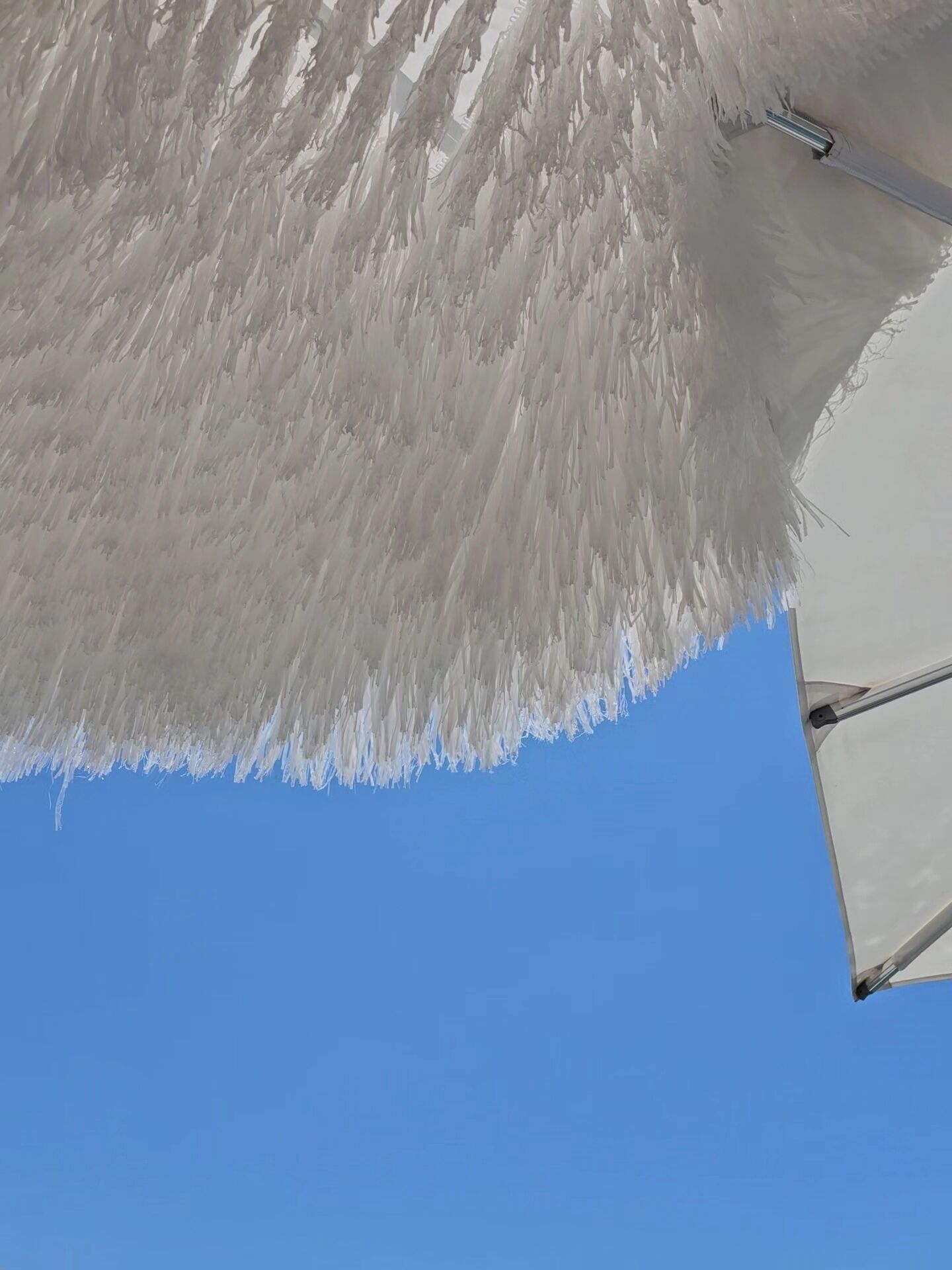 Cielo azul despejado con un objeto blanco y esponjoso, posiblemente una sombrilla de playa, parcialmente visible.