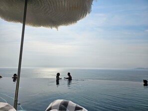 En evigheds-pool med krystalklart hav og fjerne bjerge i baggrunden.