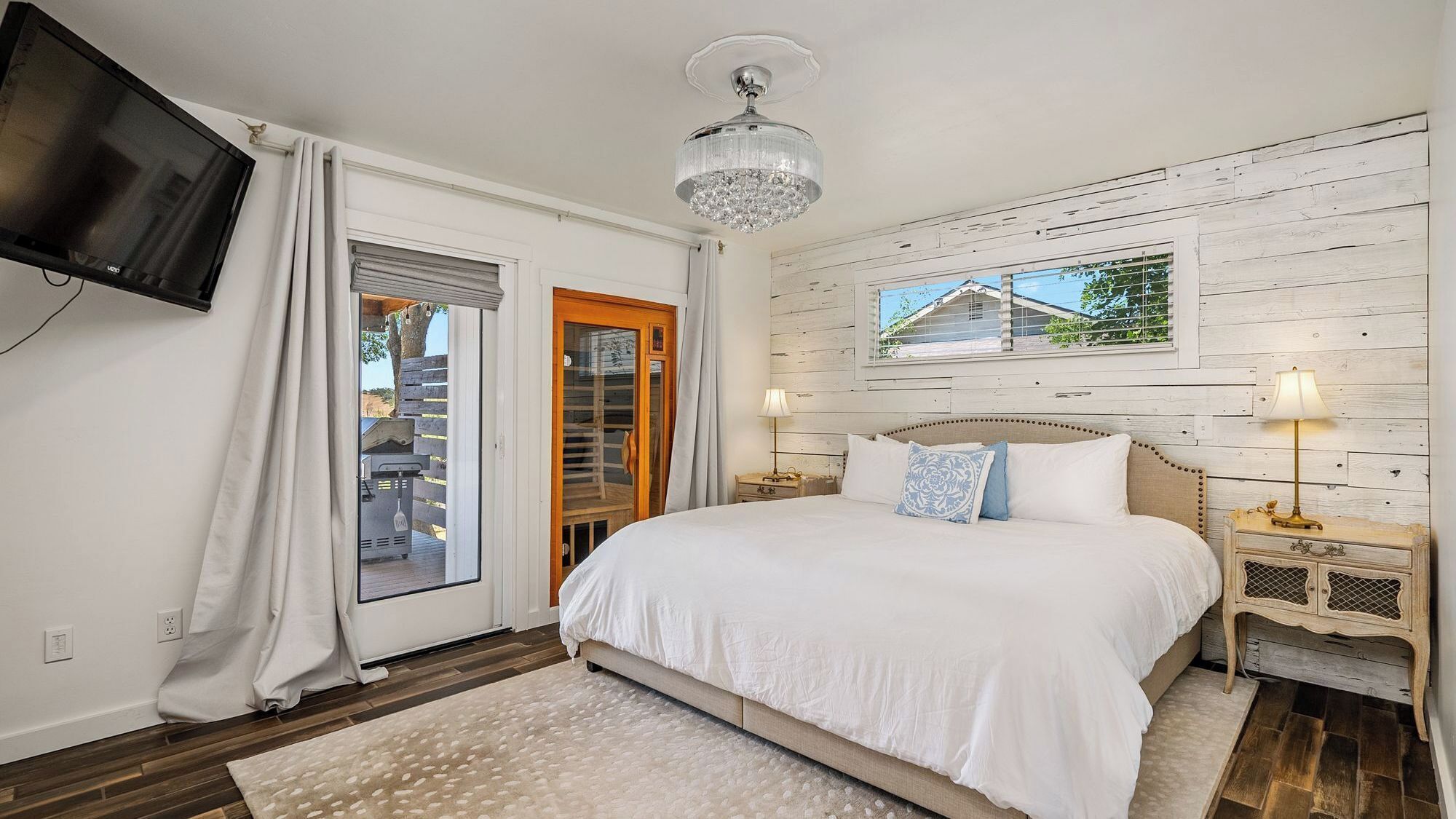 A bedroom with a large bed, a television, a chandelier, and a window with a view.