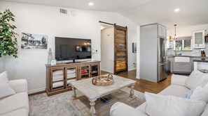 A modern living room with a flat-screen TV, a wooden entertainment unit, a coffee table, and a white sofa. - Casa Robles by Avantstay Spa + Firepit + BBQ Rural Eastside Paso Robles (Paso Robles)