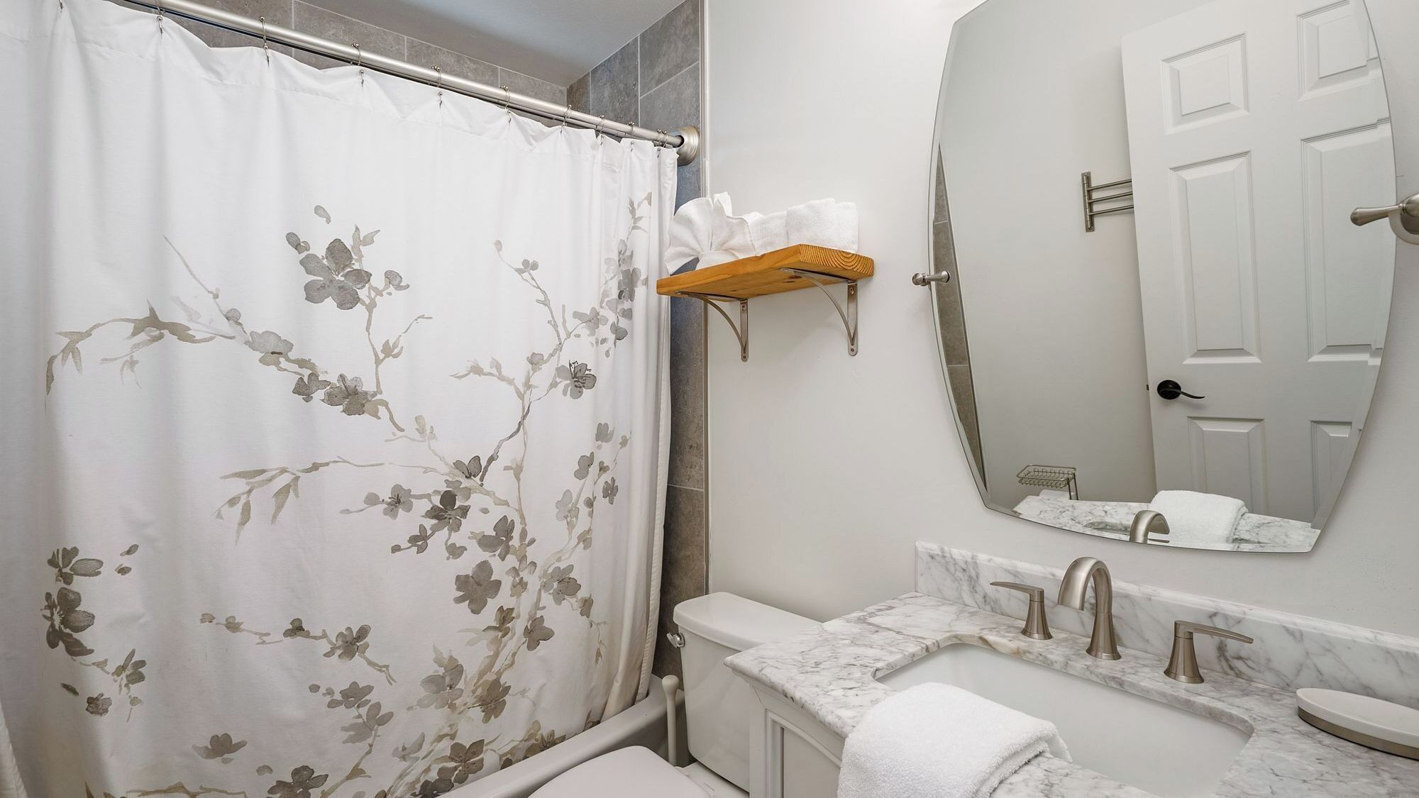 Une salle de bain équipée d’un rideau de douche, de toilettes, d’un lavabo et d’un miroir qui reflète une porte.