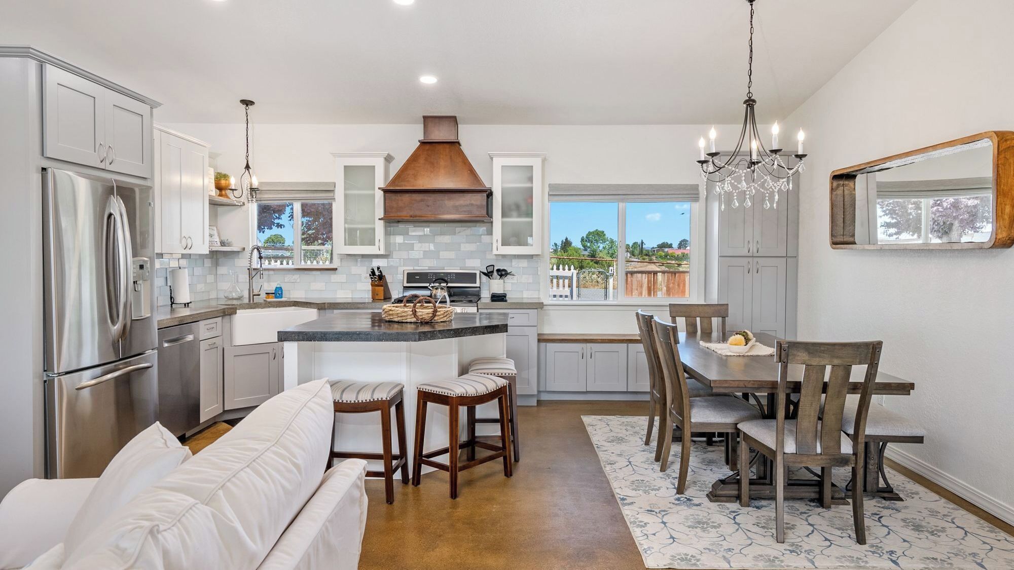 A modern kitchen with a central island, stainless steel appliances, and a dining area with wooden chairs and a white sofa.