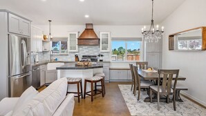A modern kitchen with a central island, stainless steel appliances, and a dining area with wooden chairs and a white sofa. - Casa Robles by Avantstay Spa + Firepit + BBQ Rural Eastside Paso Robles (Paso Robles)