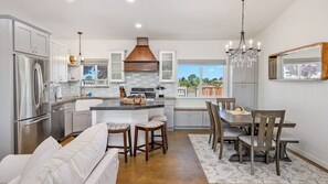 A modern kitchen with a central island, stainless steel appliances, and a dining area with wooden chairs and a white sofa. - Casa Robles by Avantstay Spa + Firepit + BBQ Rural Eastside Paso Robles (Paso Robles)