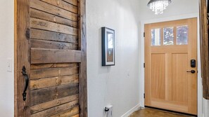 A wooden door with a black handle, a framed picture on the wall, and a light fixture above a wooden door. - Casa Robles by Avantstay Spa + Firepit + BBQ Rural Eastside Paso Robles (Paso Robles)