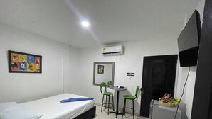 A small room with a bed, a desk, two chairs, a television, and an air conditioning unit.
