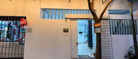 Entrada de hotel con una puerta metálica, un letrero de Coca-Cola y banderas de colores.