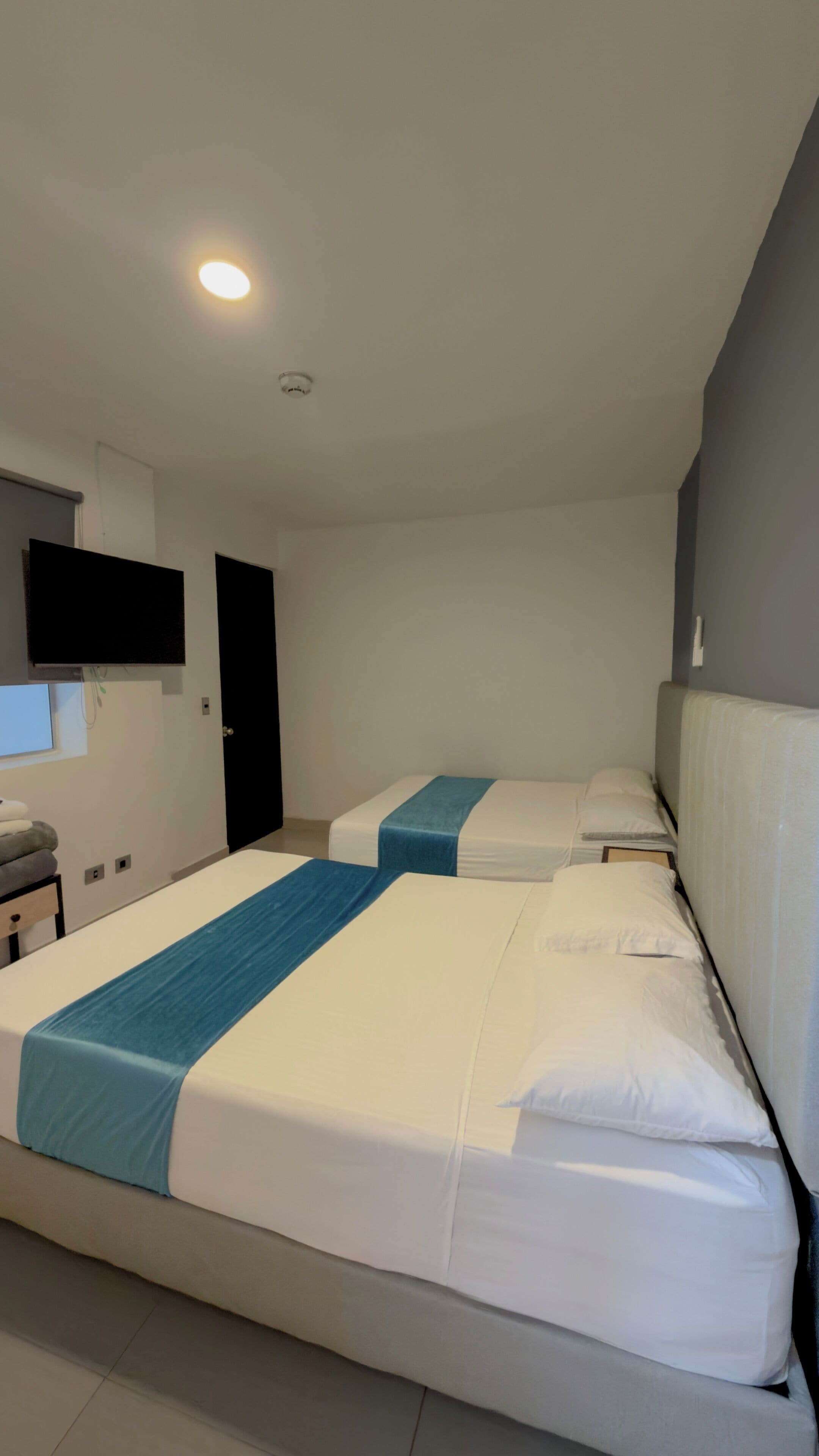 A hotel room with two beds, a flat-screen TV mounted on the wall, and a door.