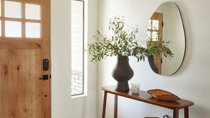 A wooden door, a vase with green plants, a round mirror, and a small table with a bowl and a glass. - Olive & Stone by Avantstay Private Acre + Hillside Views + Firepit Paso Robles (Templeton)