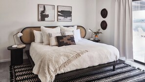 Een slaapkamer met een bed, nachtkastjes, een lamp en kunst aan de muur.