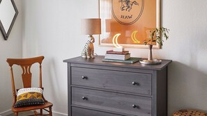 A wooden chair with a patterned cushion, a grey dresser with drawers, a lamp, books, and a framed picture with a crescent moon and the word 'HAW'. - Olive & Stone by Avantstay Private Acre + Hillside Views + Firepit Paso Robles (Templeton)