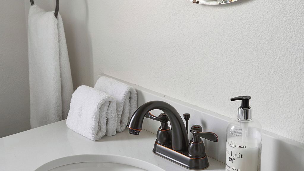 A bathroom with a white sink, a black faucet, two white towels, and a bottle of hand soap.
