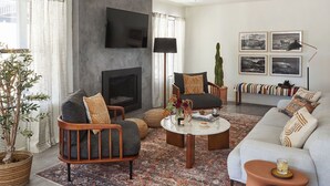A living room with a fireplace, a flat-screen TV mounted on the wall, a sofa, a coffee table, and a patterned rug. - Olive & Stone by Avantstay Private Acre + Hillside Views + Firepit Paso Robles (Templeton)