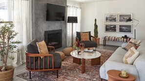 A living room with a fireplace, a flat-screen TV mounted on the wall, a sofa, a coffee table, and a patterned rug. - Olive & Stone by Avantstay Private Acre + Hillside Views + Firepit Paso Robles (Templeton)