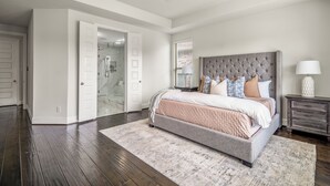 A bedroom with a large bed, a ceiling fan, a walk-in closet, and a bathroom with a glass shower. - Luxury League City Retreat (League City)