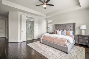 A bedroom with a large bed, a ceiling fan, a walk-in closet, and a bathroom with a glass shower. - Luxury League City Retreat (League City)