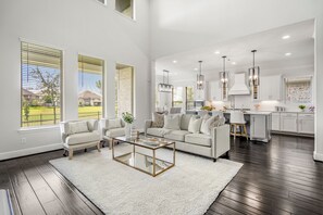 A spacious living room with a large sofa, a coffee table, and a view of the kitchen. - Luxury League City Retreat (League City)