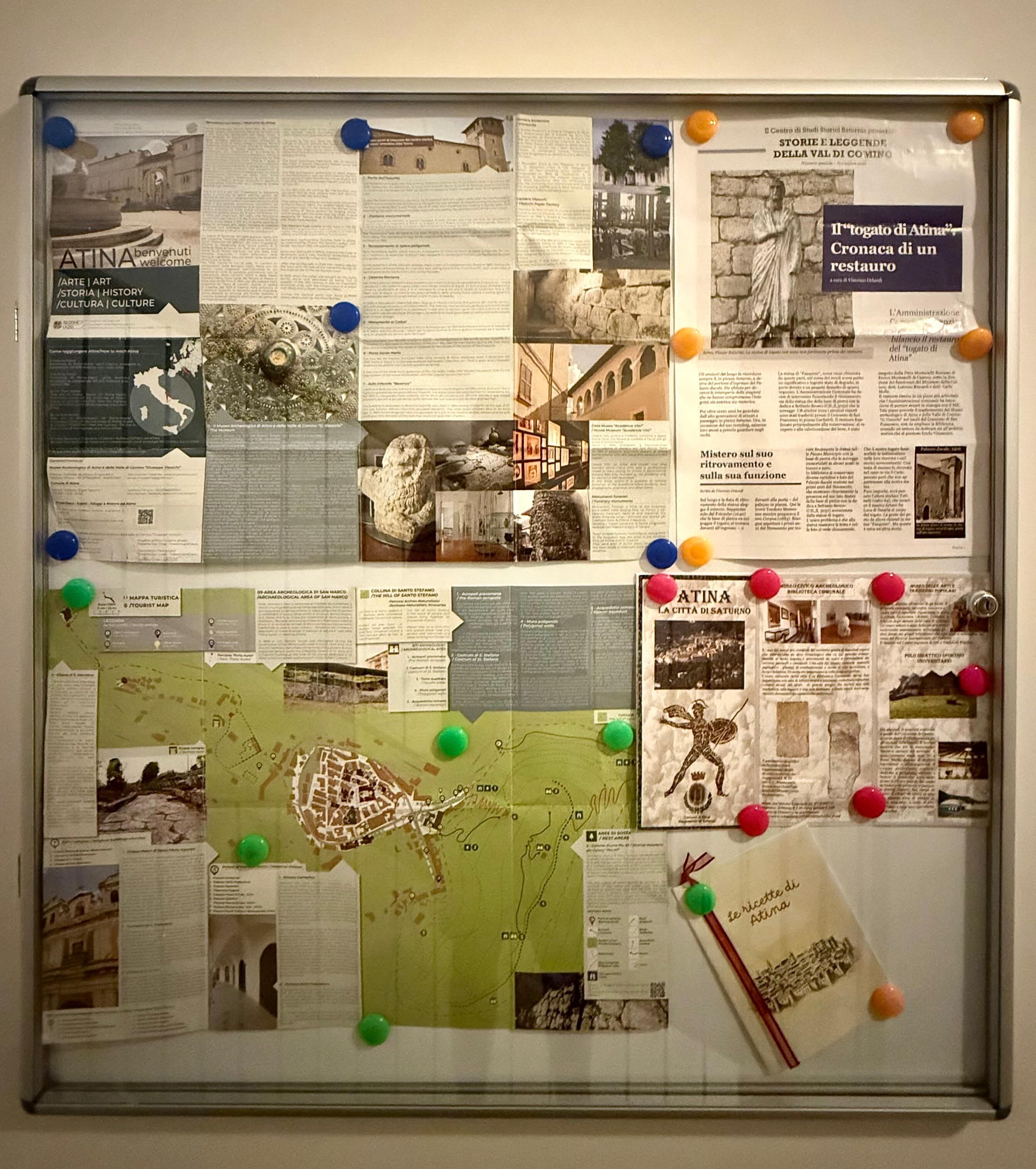 Un panneau d’affichage où sont accrochées diverses affiches d’information, des cartes et des photographies.