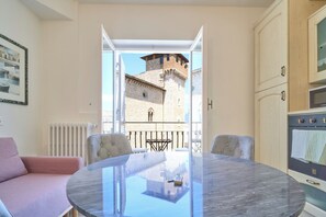 Ein Zimmer mit rundem Tisch, Stühlen, einem Heizkörper, einer Küche mit Backofen und Blick auf ein historisches Gebäude mit einem Turm.