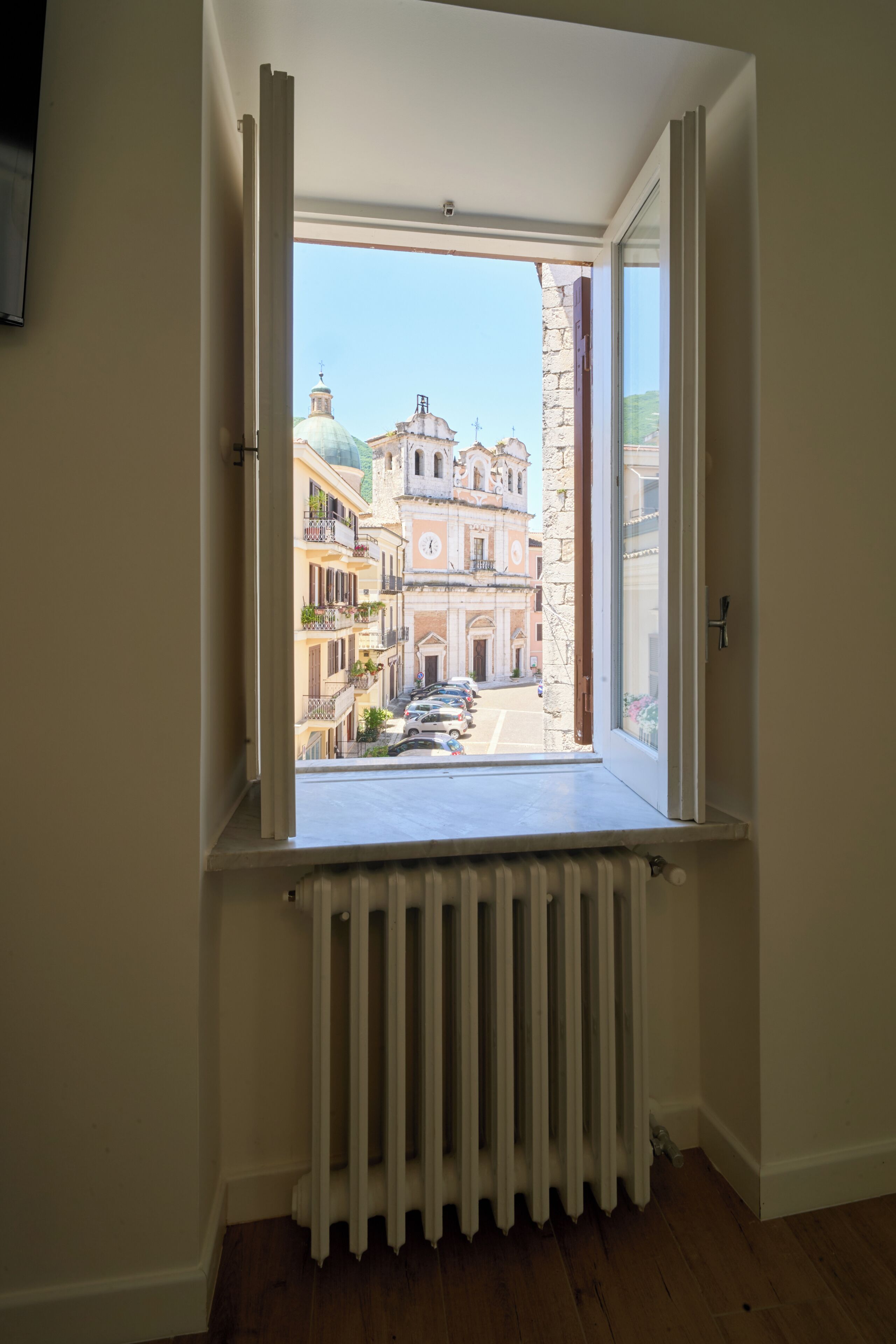 Una ventana con vistas a una calle y edificios, un radiador abajo, y una puerta a la izquierda.