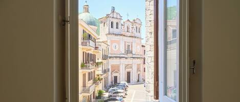 Una ventana con vistas a una calle y edificios, un radiador abajo, y una puerta a la izquierda.
