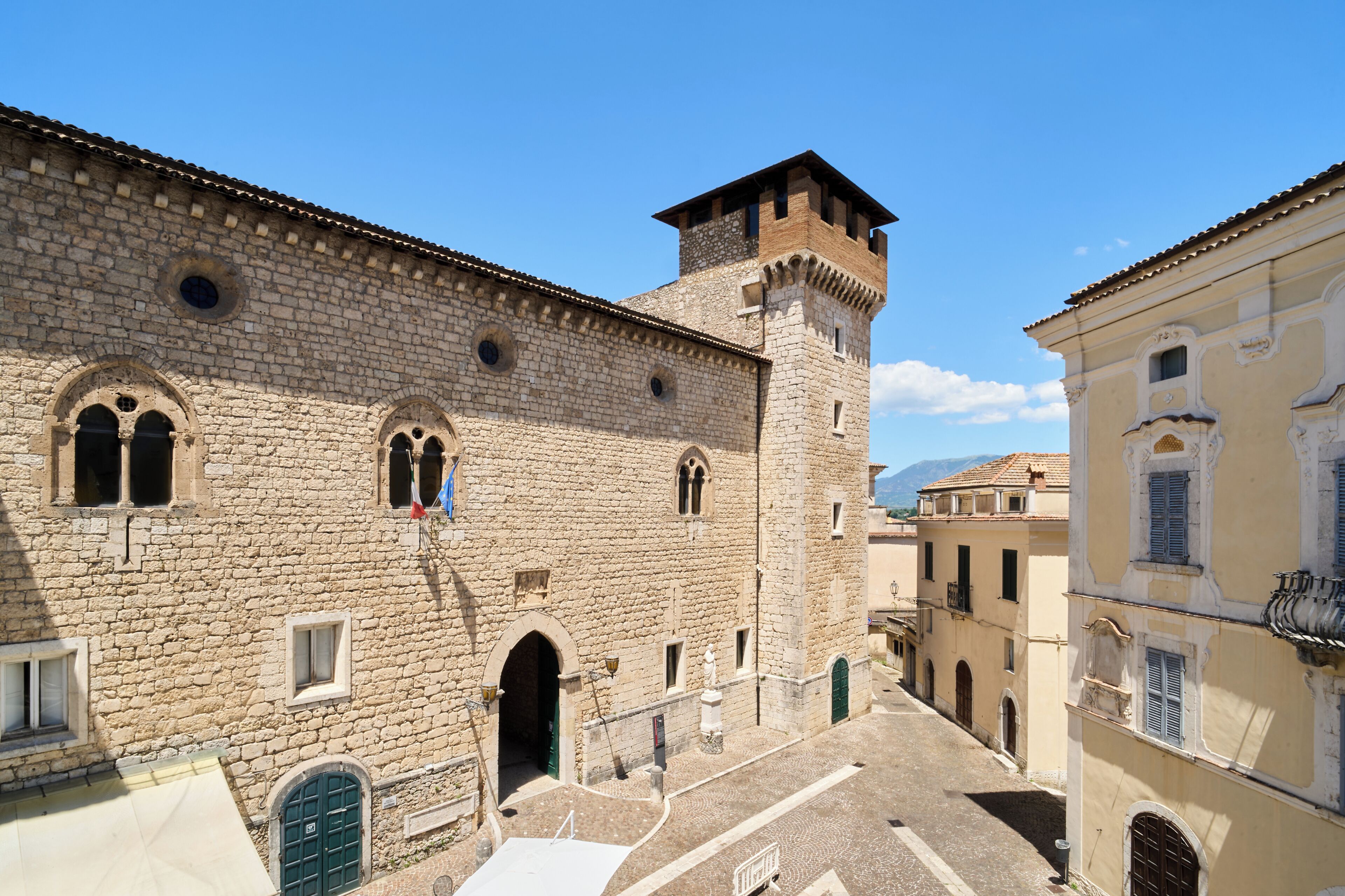 Un bâtiment historique en pierre, doté d’une tour, de fenêtres en arc et bordé d’une rue pavée.
