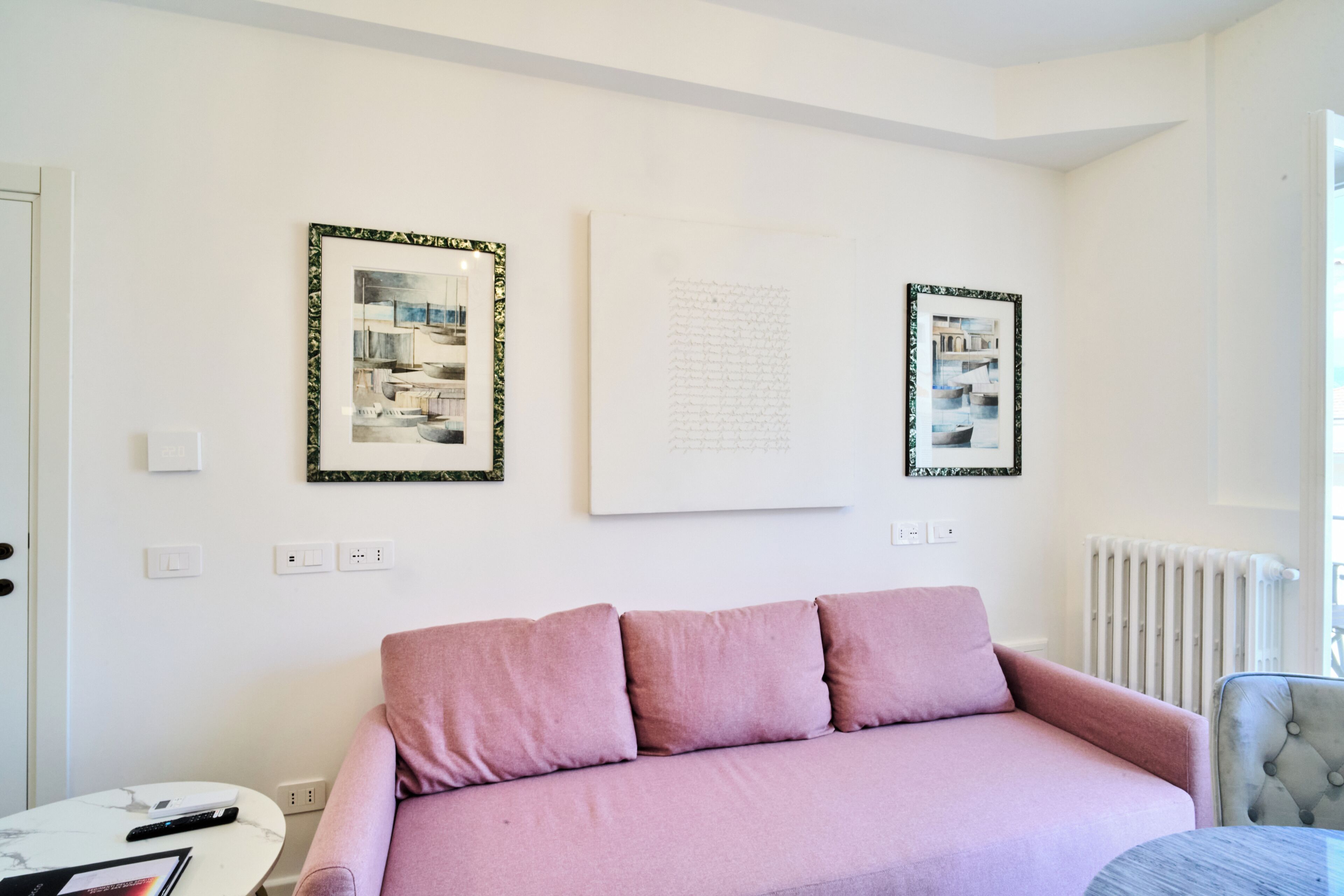 A room with a pink sofa, a small round table, and two framed artworks on the wall.