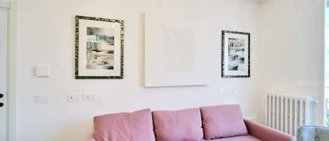 Una habitación con un sofá rosa, una mesa redonda pequeña y dos obras de arte enmarcadas en la pared.