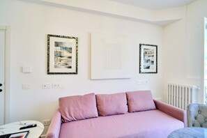 Et værelse med en lyserød sofa, et rundt bord og to billeder hængende på væggen.