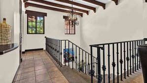 A hallway with a tiled floor, a black railing, a wooden ceiling, and a hanging light fixture. - Tropical Villa In Hacienda Pinilla (Hacienda Pinilla)