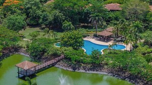 A resort with a swimming pool surrounded by lush greenery and a bridge leading to a gazebo. - Tropical Villa In Hacienda Pinilla (Hacienda Pinilla)