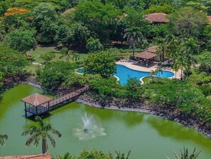 Ein Resort mit Schwimmbad, umgeben von üppiger Vegetation und einer Brücke zu einem Pavillon.