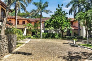 A courtyard with cobblestone flooring, palm trees, and a building with a tiled roof. - Tropical Villa In Hacienda Pinilla (Hacienda Pinilla)