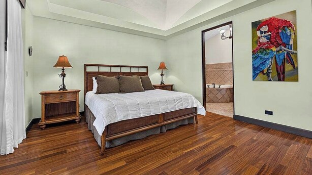 A bedroom with a wooden bed, two bedside tables with lamps, a large window, and a door leading to a bathroom. - Tropical Villa In Hacienda Pinilla (Hacienda Pinilla)