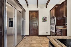 A kitchen with stainless steel appliances, wooden cabinets, and a tiled floor. - Tropical Villa In Hacienda Pinilla (Hacienda Pinilla)