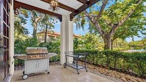 An outdoor patio with a grill and a cart, surrounded by greenery and a view of a residential area. - Tropical Villa In Hacienda Pinilla (Hacienda Pinilla)
