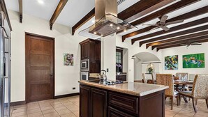 A kitchen with a central island, wooden ceiling beams, and a dining area with wicker chairs. - Tropical Villa In Hacienda Pinilla (Hacienda Pinilla)