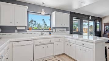 A kitchen with white cabinets, a large window, and a view of the outdoors.