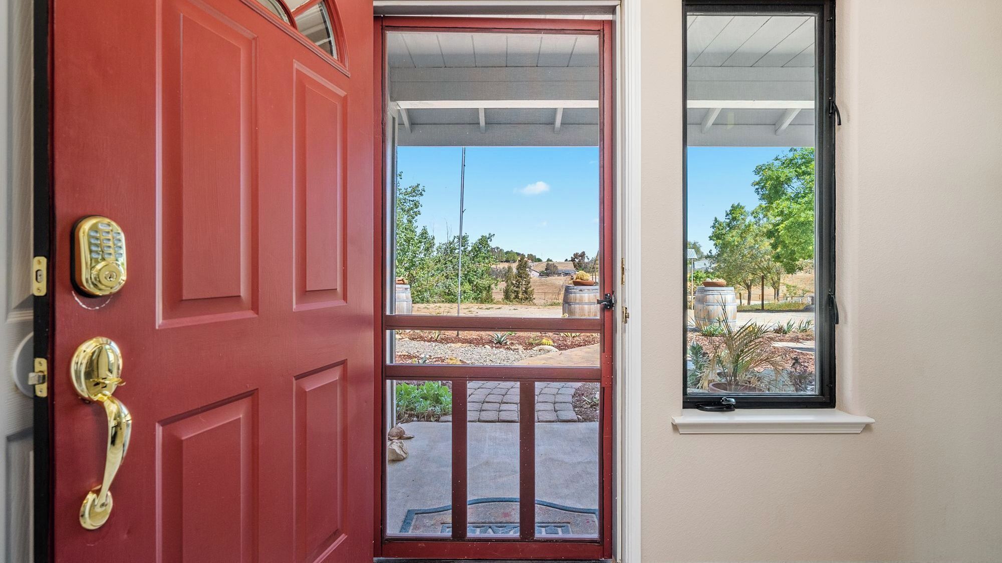 A red door with a keypad lock and a window with a view of a garden.