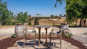 An outdoor seating area with a round table and two chairs, surrounded by wooden barrels and a pergola. - Casa Merlot by Avantstay Pool Table + Firepit + BBQ Eastside Paso Wine Country (Paso Robles)