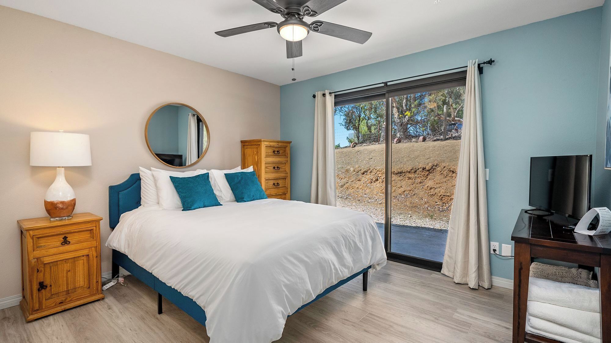 A bedroom with a bed, a nightstand, a dresser, a ceiling fan, a television, and a sliding glass door leading to an outdoor area.