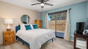 Ein Schlafzimmer mit Bett, Nachttisch, Kommode, Deckenventilator, Fernseher und einer Schiebetür zu einem Außenbereich.