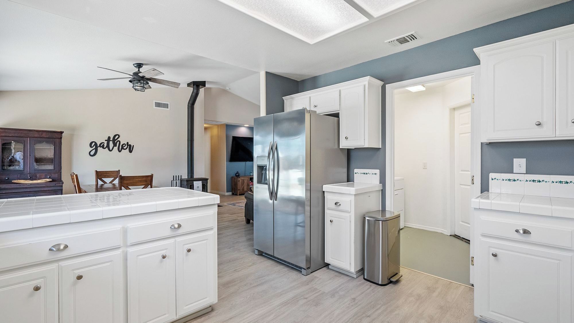 A modern kitchen with white cabinetry, a stainless steel refrigerator, and a dining area with a wooden table and chairs.