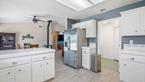 A modern kitchen with white cabinetry, a stainless steel refrigerator, and a dining area with a wooden table and chairs. - Casa Merlot by Avantstay Pool Table + Firepit + BBQ Eastside Paso Wine Country (Paso Robles)