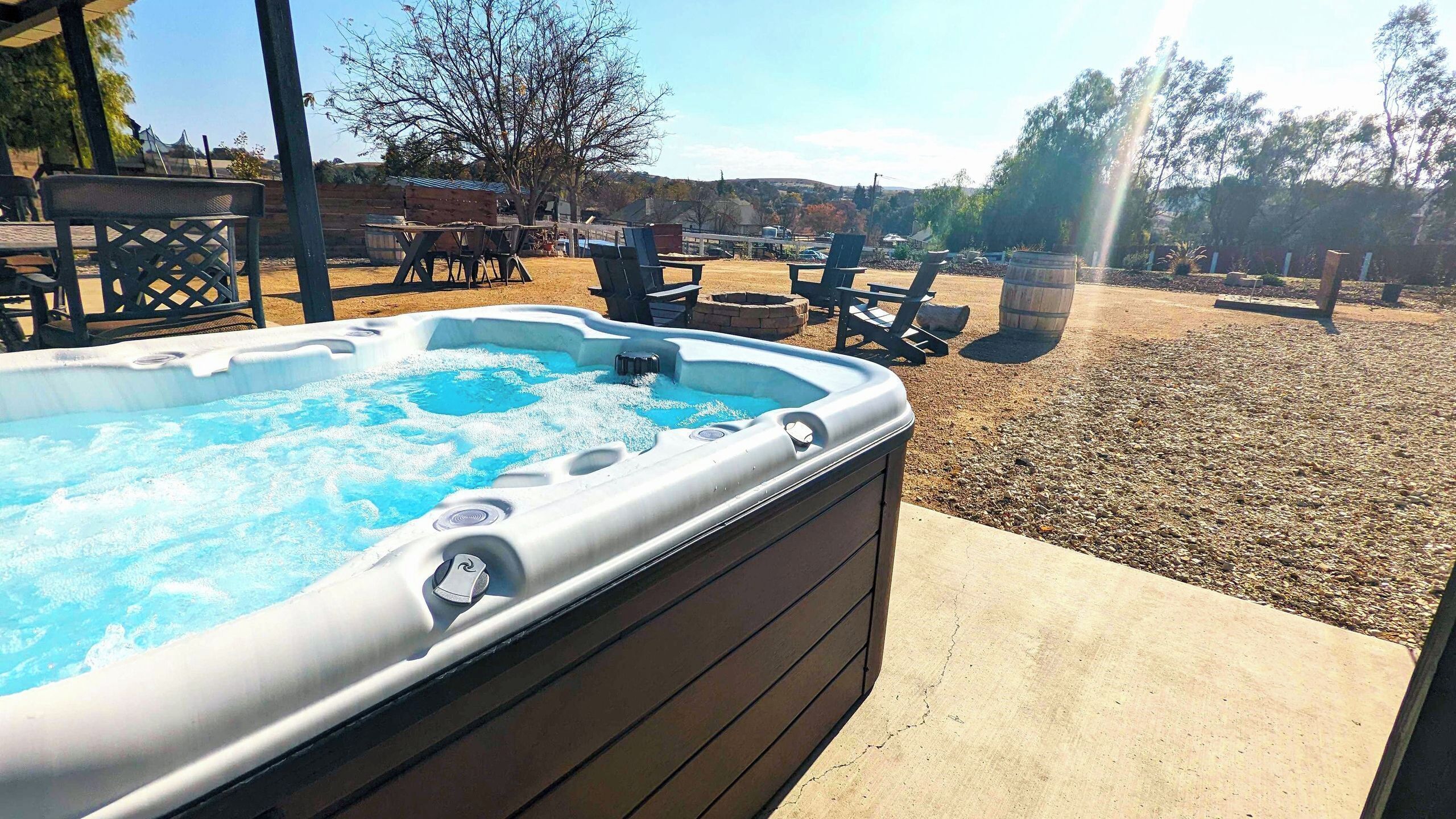 A hot tub with a wooden deck, surrounded by outdoor furniture and a gravel area.
