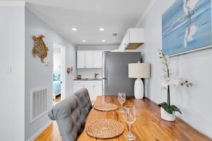 A modern kitchen with white cabinets, a grey refrigerator, and a dining area with a wooden table and grey upholstered chairs. - Old Town Apartment with Parking, Walk to the Beach (Key West)