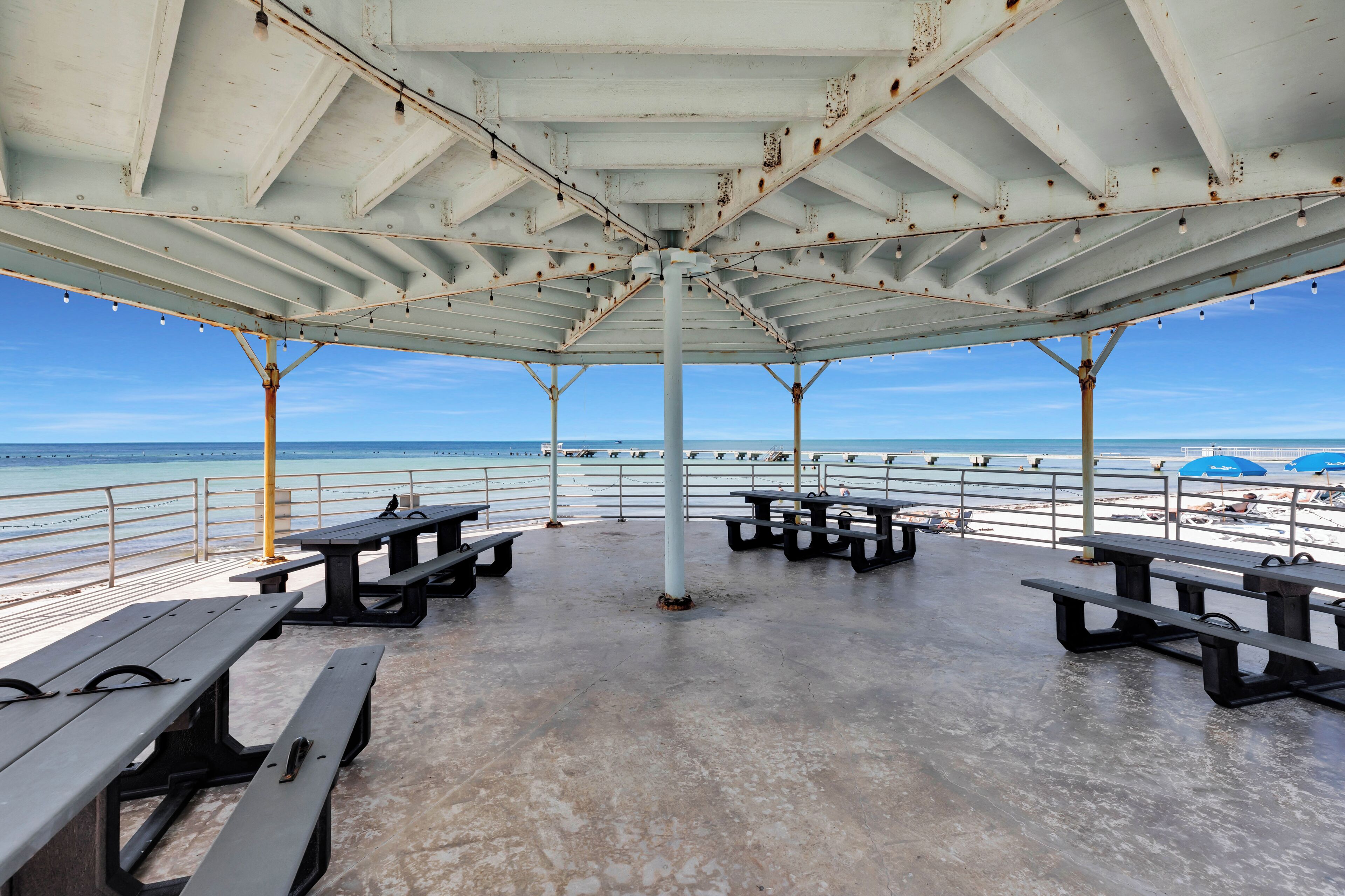 A covered outdoor seating area with picnic tables and a view of the beach.