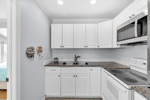 A modern kitchen with white cabinetry, a stainless steel sink, a microwave, and a stove. - Old Town Apartment with Parking, Walk to the Beach (Key West)
