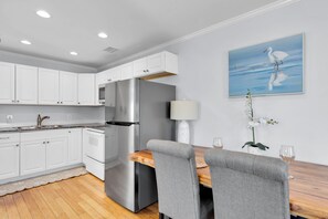 A modern kitchen with white cabinets, a stainless steel refrigerator, and a dining area with a table and chairs. - Old Town Apartment with Parking, Walk to the Beach (Key West)