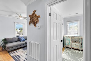 A room with a grey sofa, a decorative wall piece, a ceiling fan, and a white door leading to another room. - Old Town Apartment with Parking, Walk to the Beach (Key West)